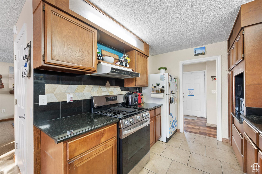 Kitchen featuring dark stone countertops, stainless steel gas range, exhaust hood, light tile floors, and tasteful backsplash
