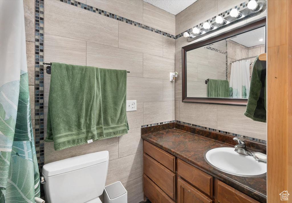 Bathroom with toilet, vanity, tile walls, and a textured ceiling