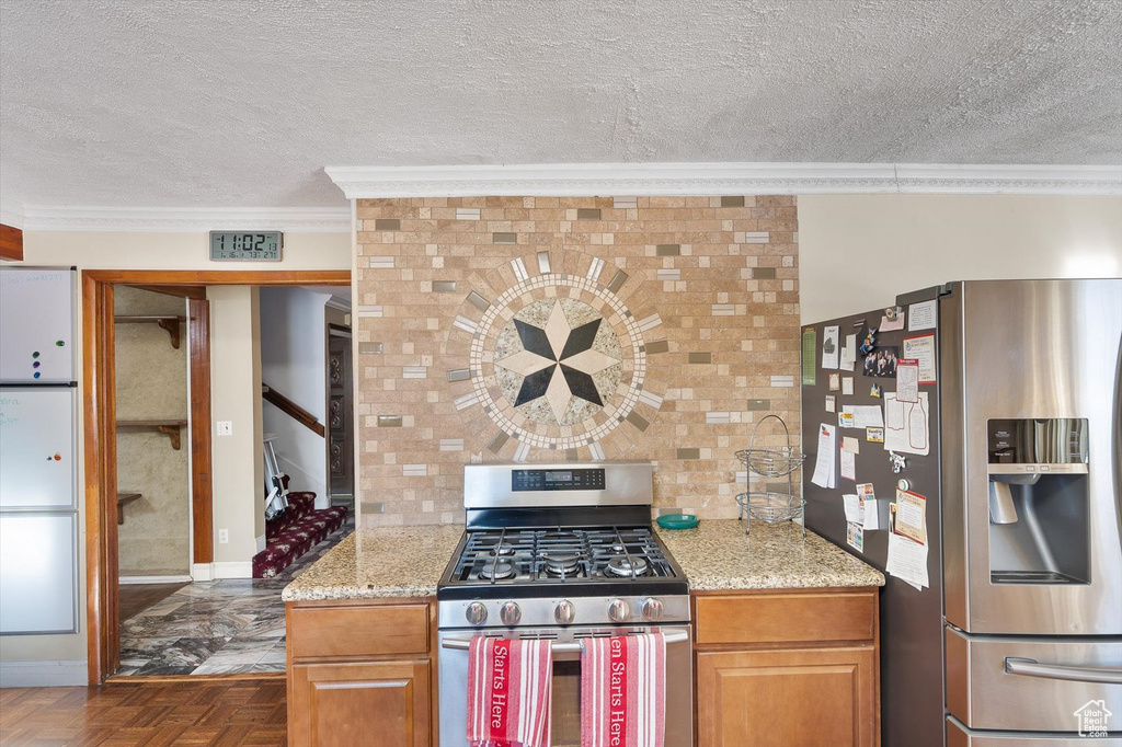 Kitchen with appliances with stainless steel finishes, dark parquet flooring, a textured ceiling, and light stone countertops