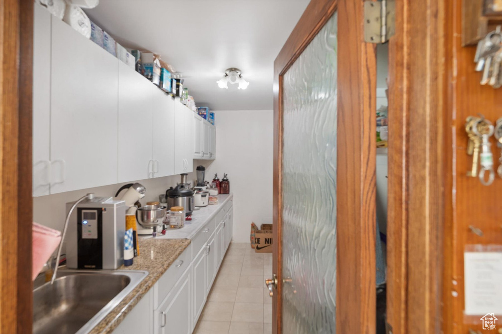 Kitchen featuring white cabinets, sink, light stone countertops, and light tile flooring