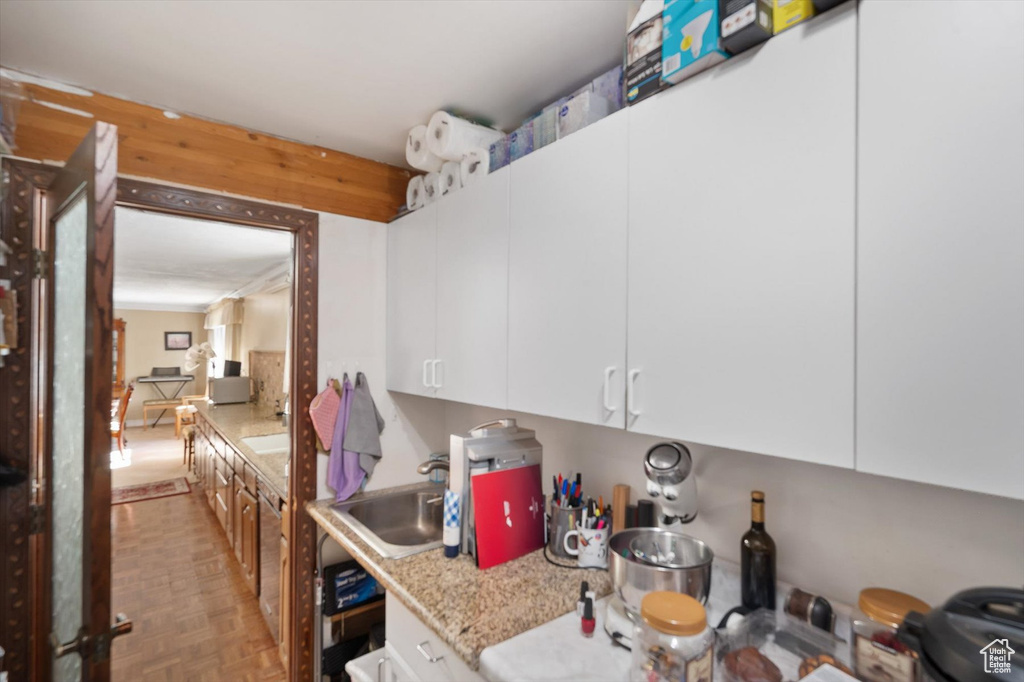 Kitchen featuring sink, light parquet flooring, light stone countertops, and white cabinets