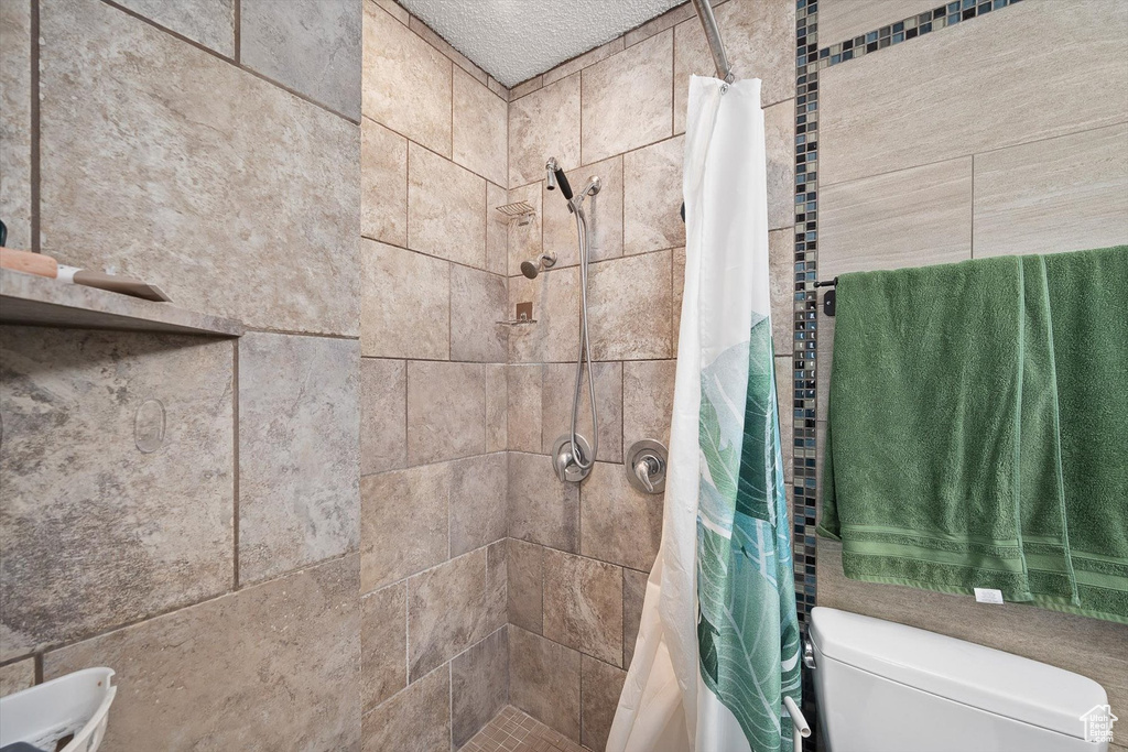 Bathroom featuring toilet, a shower with curtain, and a textured ceiling