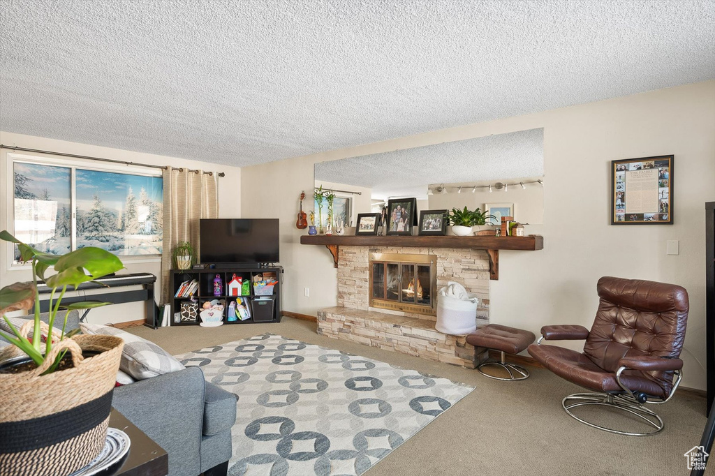Carpeted living room featuring a stone fireplace and a textured ceiling