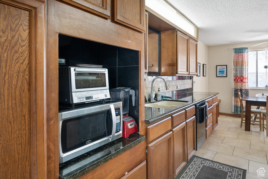 Kitchen featuring light tile floors, backsplash, dishwasher, sink, and a textured ceiling