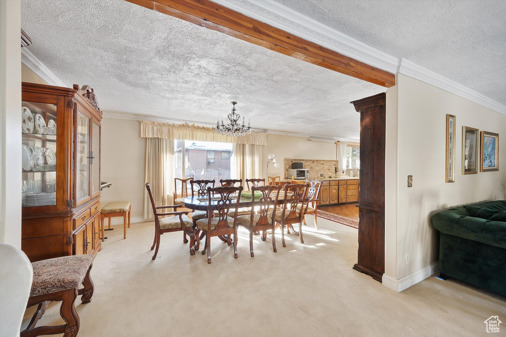 Carpeted dining room with a notable chandelier, ornamental molding, and a textured ceiling