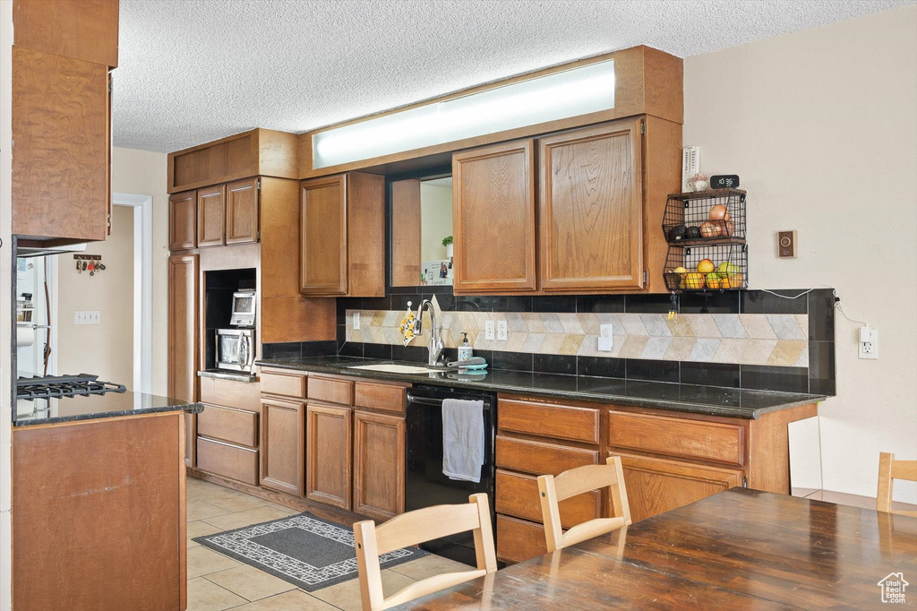 Kitchen featuring light tile floors, tasteful backsplash, dishwasher, sink, and a textured ceiling