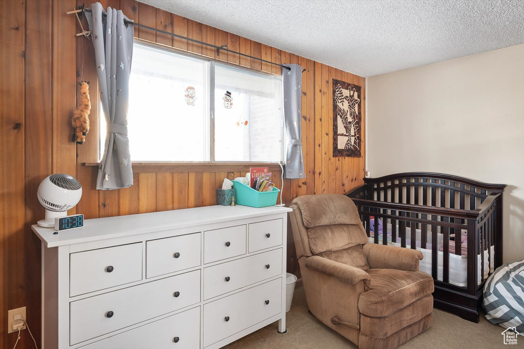 Carpeted bedroom featuring wood walls, a crib, and a textured ceiling
