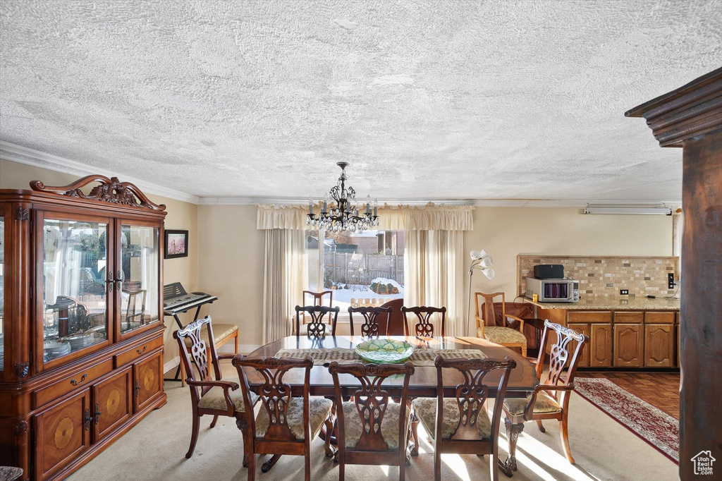Carpeted dining room with a chandelier, crown molding, a textured ceiling, and decorative columns