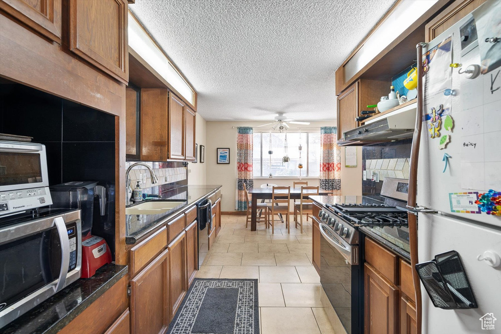 Kitchen featuring appliances with stainless steel finishes, a textured ceiling, light tile floors, ceiling fan, and sink