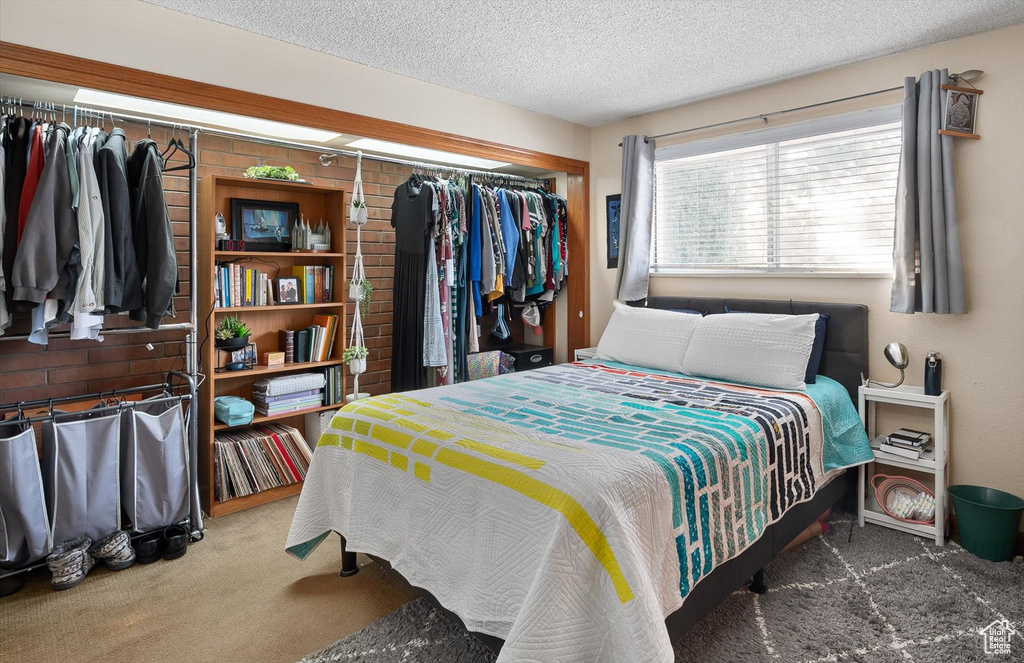 Bedroom with a textured ceiling, a closet, dark colored carpet, and brick wall