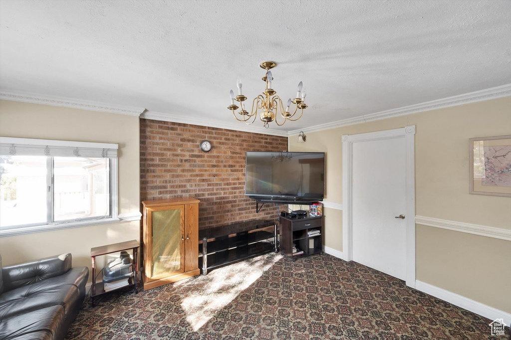Living room featuring crown molding, a notable chandelier, brick wall, dark carpet, and a textured ceiling