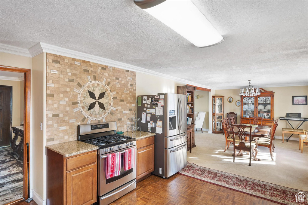 Kitchen featuring stainless steel appliances, light parquet floors, light stone counters, a notable chandelier, and a textured ceiling