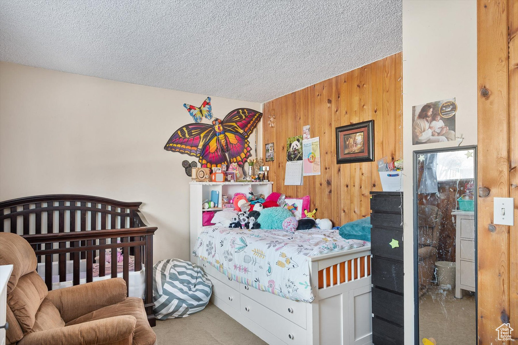 Bedroom with light colored carpet, wood walls, and a textured ceiling