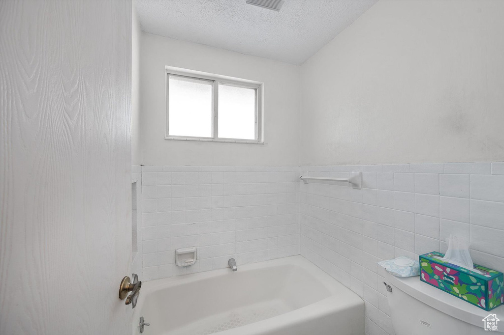 Bathroom with toilet, shower / bathing tub combination, tile walls, and a textured ceiling