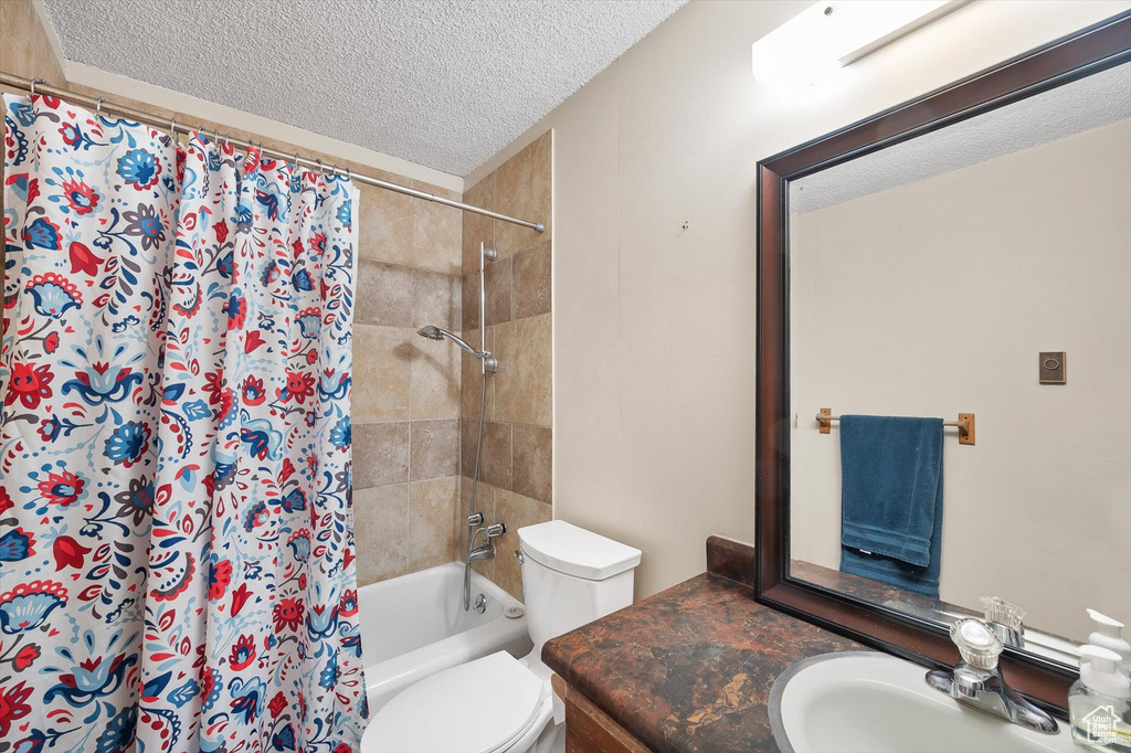 Full bathroom with a textured ceiling, large vanity, shower / bathtub combination with curtain, and toilet