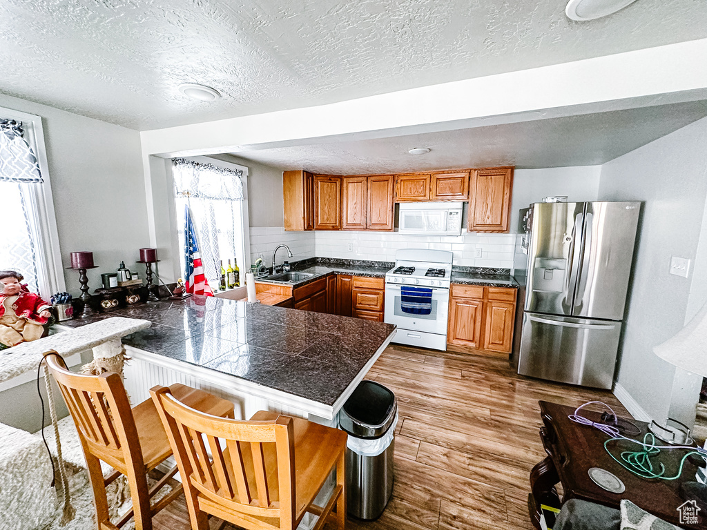Kitchen featuring light hardwood / wood-style floors, tasteful backsplash, white appliances, sink, and a textured ceiling