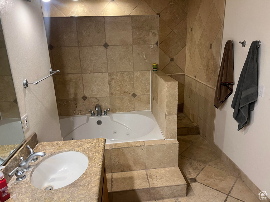 Bathroom featuring tiled tub, vanity, and tile flooring