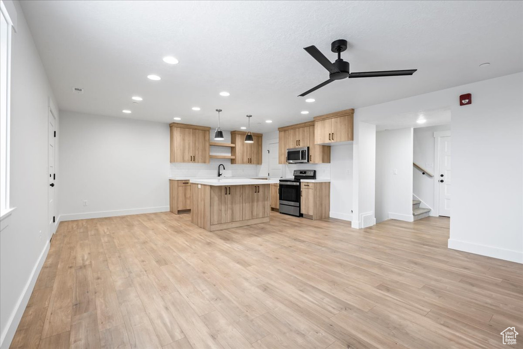 Kitchen featuring a kitchen island, ceiling fan, hanging light fixtures, appliances with stainless steel finishes, and light hardwood / wood-style flooring