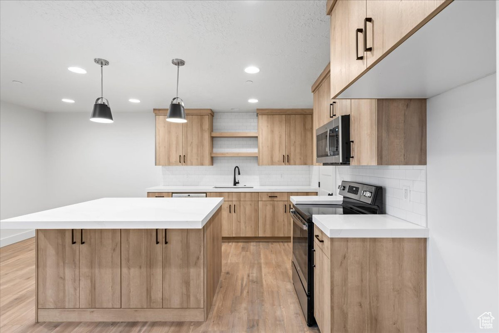 Kitchen with decorative light fixtures, light hardwood / wood-style flooring, stainless steel appliances, sink, and tasteful backsplash