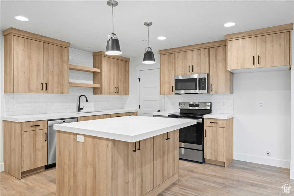 Kitchen with tasteful backsplash, light wood-type flooring, appliances with stainless steel finishes, decorative light fixtures, and a center island