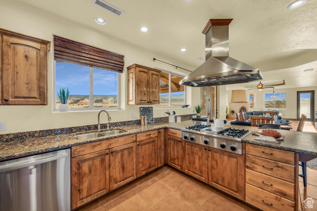 Kitchen with appliances with stainless steel finishes, plenty of natural light, dark stone counters, and island range hood