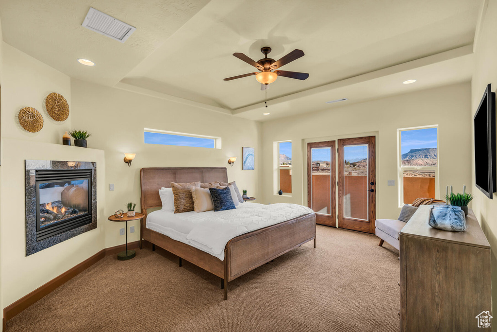 Carpeted bedroom featuring ceiling fan, a raised ceiling, and access to outside