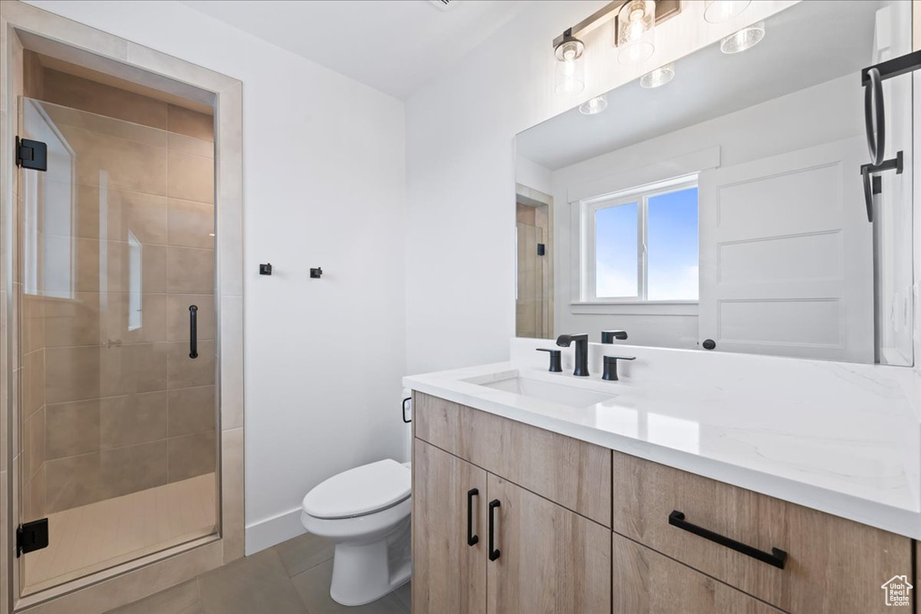 Bathroom featuring toilet, vanity, a shower with door, and tile flooring