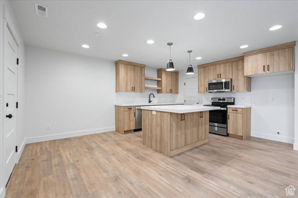 Kitchen with stainless steel appliances, decorative light fixtures, backsplash, light hardwood / wood-style flooring, and a center island