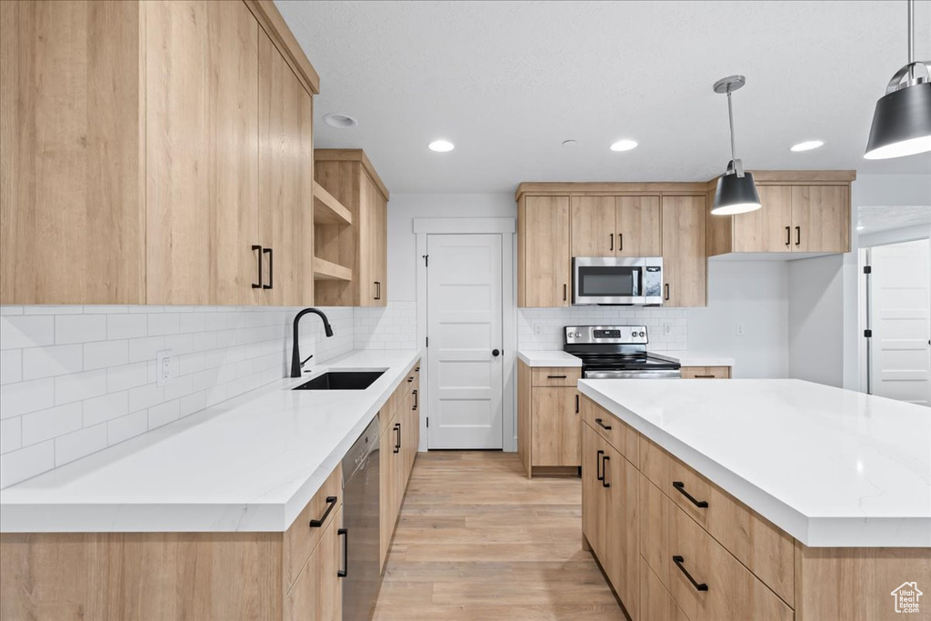 Kitchen with light hardwood / wood-style floors, tasteful backsplash, hanging light fixtures, sink, and stainless steel appliances