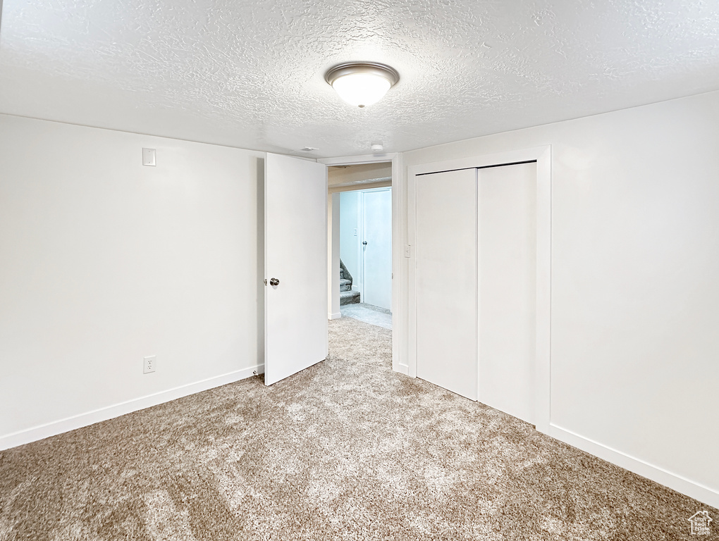 Unfurnished bedroom featuring light colored carpet, a closet, and a textured ceiling