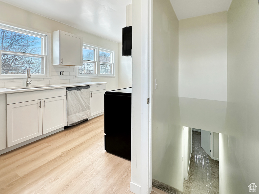 Kitchen featuring white cabinetry, stainless steel dishwasher, backsplash, light hardwood / wood-style flooring, and sink