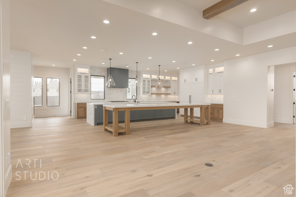 Kitchen with a breakfast bar area, decorative light fixtures, white cabinets, light hardwood / wood-style flooring, and a kitchen island with sink