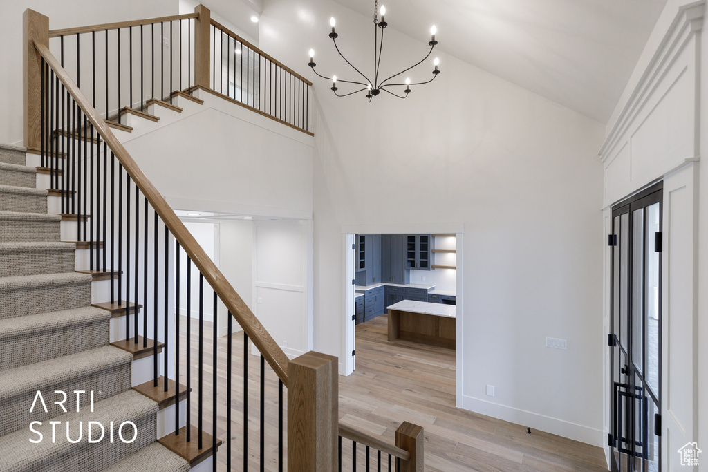 Staircase with a chandelier, high vaulted ceiling, and light hardwood / wood-style flooring