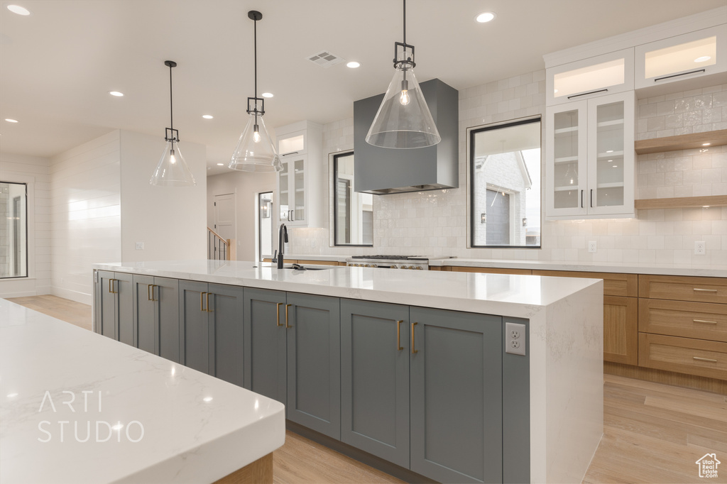 Kitchen with light wood-type flooring, pendant lighting, gray cabinets, and a center island with sink
