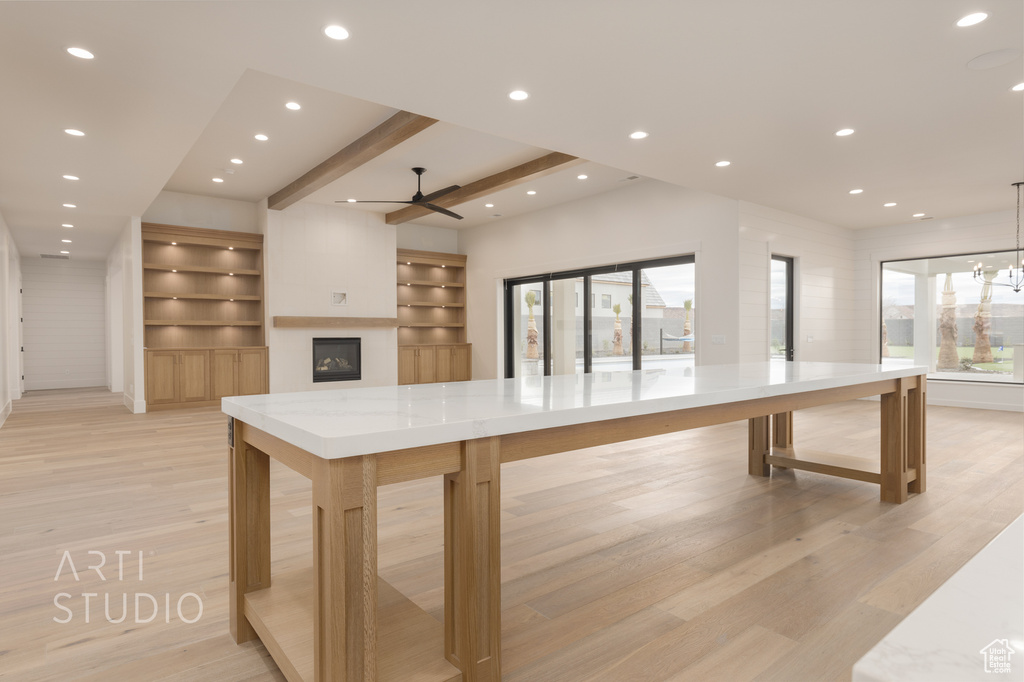 Kitchen featuring light stone countertops, ceiling fan with notable chandelier, light hardwood / wood-style floors, beamed ceiling, and pendant lighting