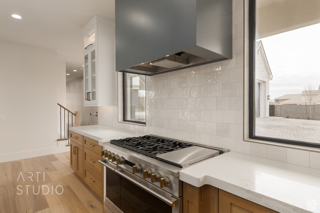 Kitchen with light hardwood / wood-style floors, high end range, backsplash, white cabinets, and wall chimney range hood