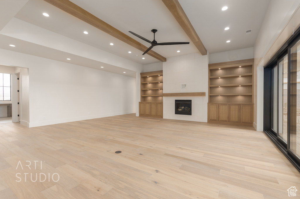 Unfurnished living room featuring light hardwood / wood-style flooring, built in shelves, beamed ceiling, and ceiling fan
