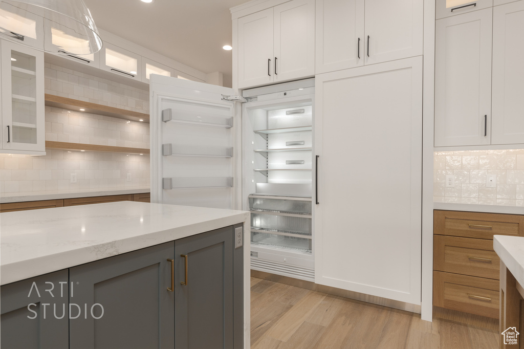 Kitchen with tasteful backsplash, white cabinets, light hardwood / wood-style floors, and light stone counters