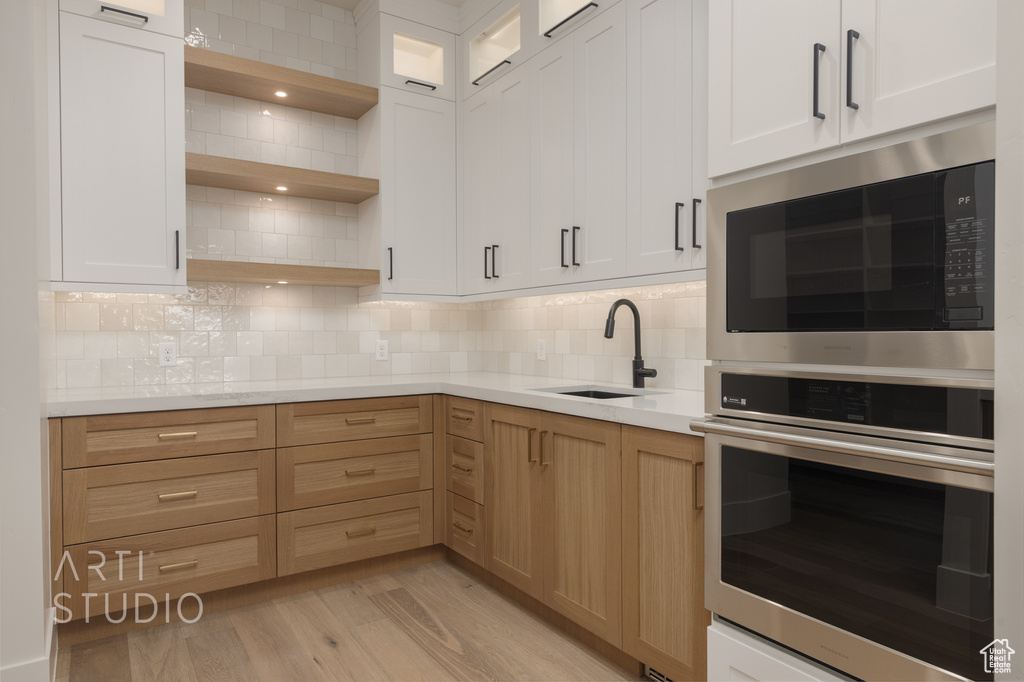 Kitchen with black microwave, light hardwood / wood-style flooring, backsplash, sink, and white cabinetry