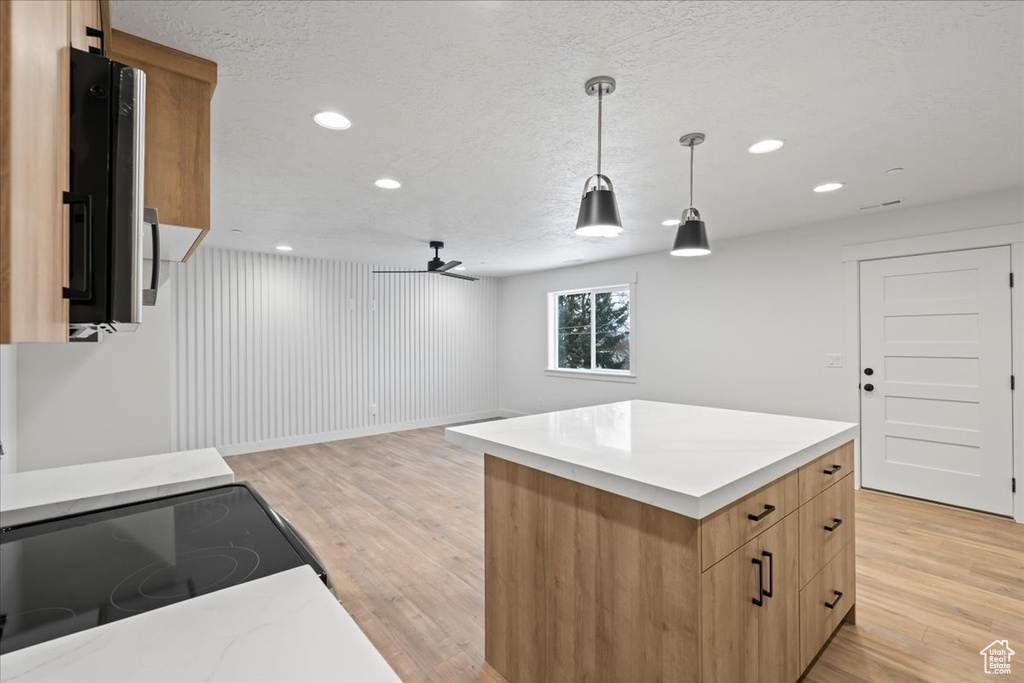 Kitchen with light hardwood / wood-style floors, a kitchen island, ceiling fan, pendant lighting, and a textured ceiling