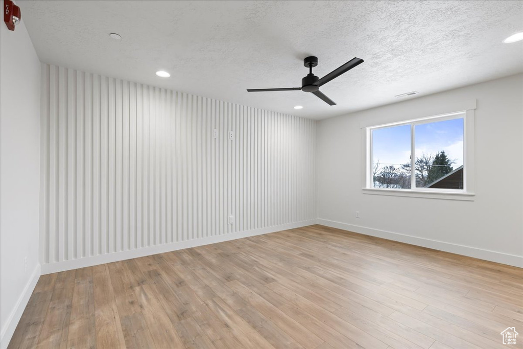 Empty room featuring light wood-type flooring, a textured ceiling, and ceiling fan