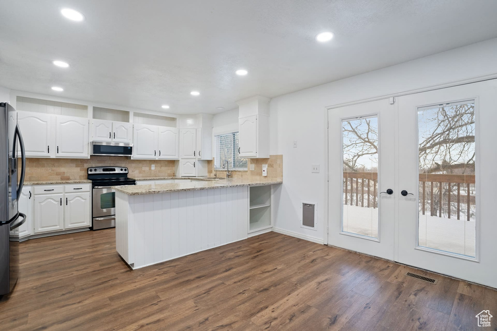 Kitchen featuring light stone countertops, appliances with stainless steel finishes, kitchen peninsula, dark hardwood / wood-style floors, and white cabinets