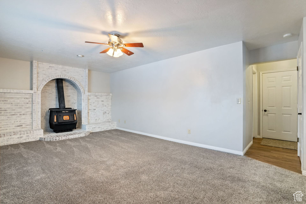Unfurnished living room featuring a wood stove, carpet floors, and ceiling fan