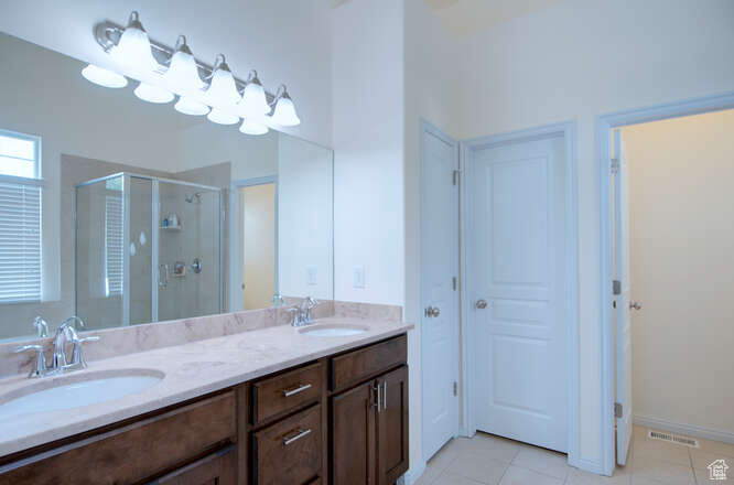 Bathroom with a shower with shower door, double sink vanity, and tile flooring