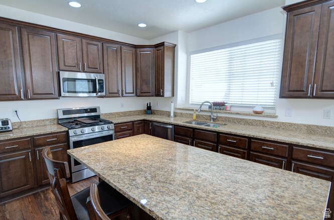 Kitchen with sink, appliances with stainless steel finishes, and light stone counters