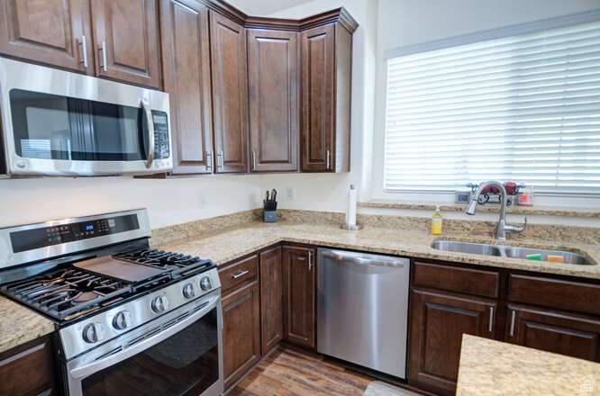 Kitchen featuring sink, stainless steel appliances, light hardwood / wood-style floors, and light stone countertops