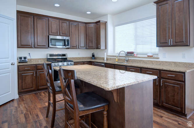 Kitchen with a kitchen breakfast bar, appliances with stainless steel finishes, dark hardwood / wood-style floors, sink, and a center island