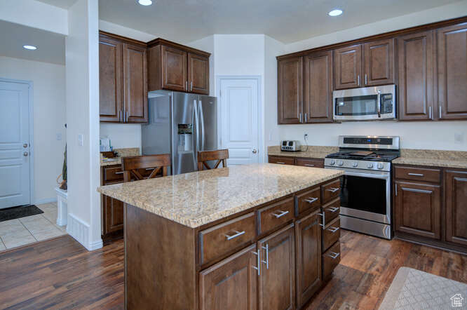 Kitchen with a kitchen island, appliances with stainless steel finishes, light stone countertops, and dark wood-type flooring
