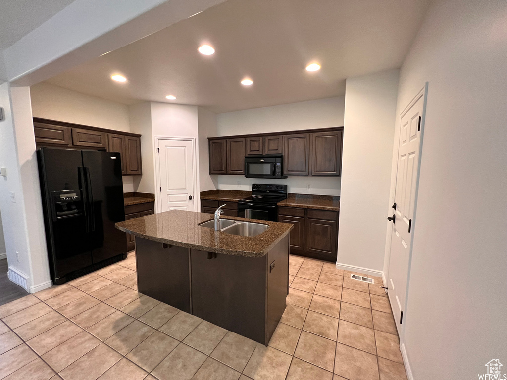 Kitchen with an island with sink, dark stone counters, black appliances, and light tile floors