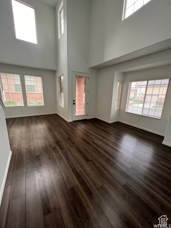 Empty room featuring dark hardwood / wood-style flooring, a towering ceiling, and a wealth of natural light